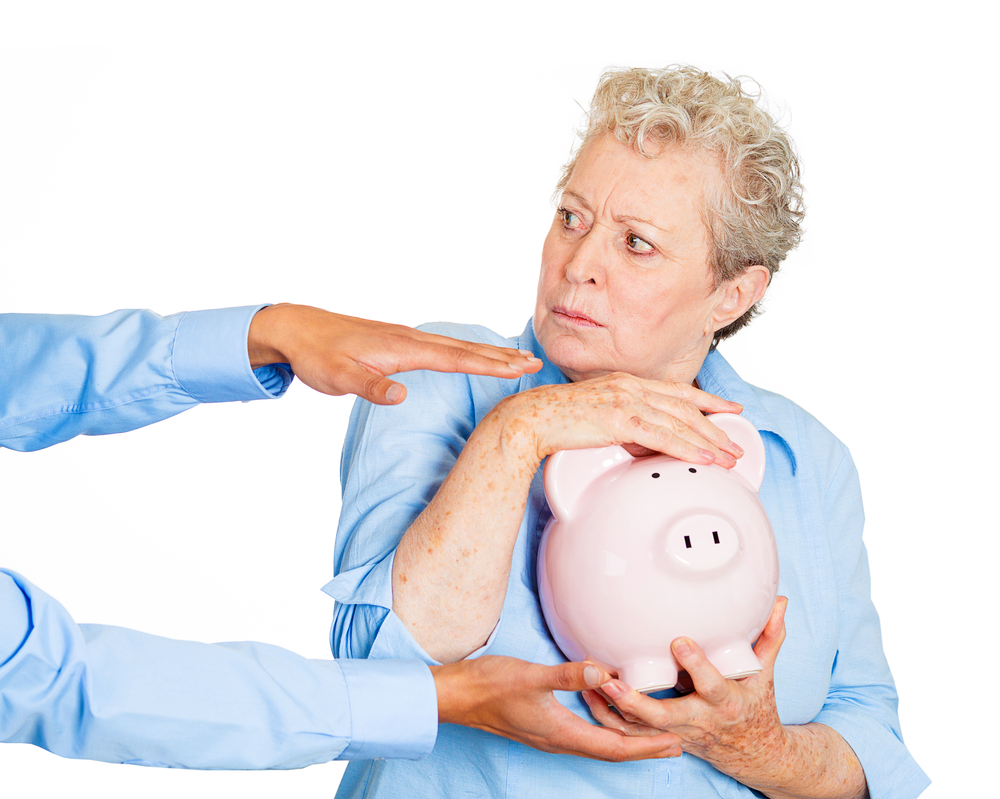 Senior woman protectively holding piggy bank someone else tries to reach.